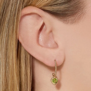 Detalle de pendiente de aro dorado con colgante de gema verde en forma de corazón en modelo