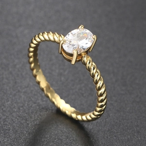 Macro detail of oval cut zircon with a golden rope twist band on a dark textured background