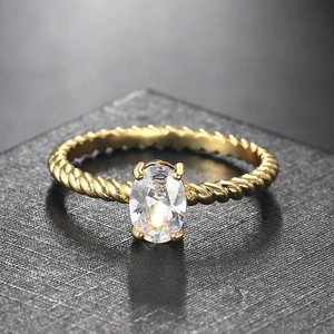 Detailed close-up of a gold twist band ring featuring a clear oval cubic zirconia stone