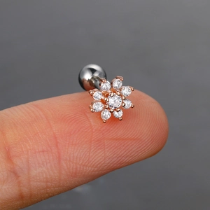 Primer plano de un pendiente de flor en oro rosa con circón sostenido en la yema del dedo