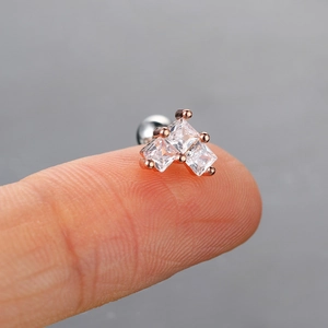 Vista macro de pendientes de oro rosa con tres circonitas cuadradas sobre el dedo