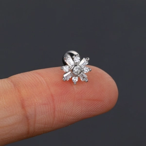 Sparkling silver snowflake ear stud with cubic zirconia held by hand against dark background
