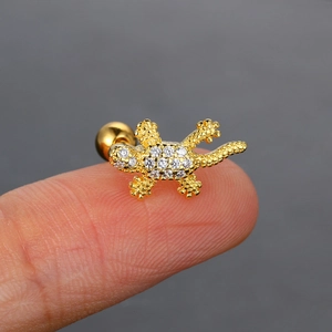 Primer plano macro de un pequeño pendiente de lagarto dorado con circonitas en el dedo