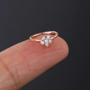 Macro shot of a rose gold flower nose ring with white zircon stones held on a fingertip