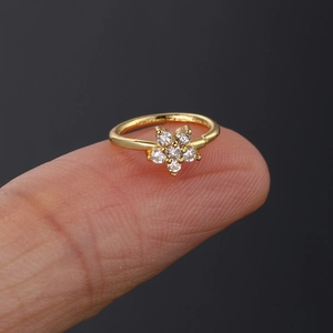 Macro view of a gold-plated flower nose ring with white zircon stones held on a fingertip