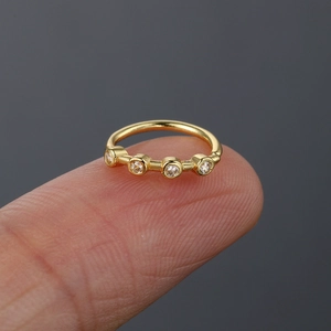 Macro shot of a tiny gold nose ring with four inlaid zircons shown on a fingertip