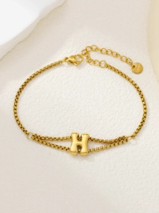 Detailopname van de gouden letter H bedel op een roestvrijstalen vierkante schakelarmband