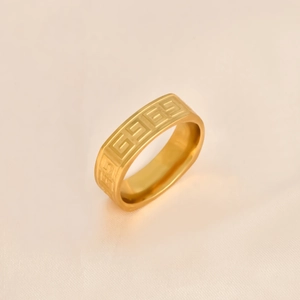 Macro detail of gold stainless steel ring featuring Greek key patterns on silk fabric