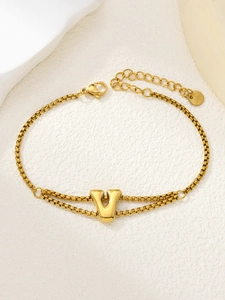 Detail van vergulde dubbellaagse armband met een centrale letter V hanger en karabijnslot
