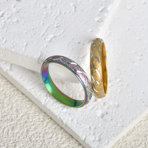 Detail showing rainbow and gold twisted texture rings on white stone background