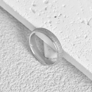 Macro detail of silver frosted stainless steel ring on a white textured stone base