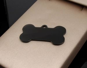 Close-up of matte black bone-shaped stainless steel pet ID tag on silk fabric