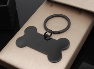 Detailed view of bone-shaped black matte stainless steel pet tag on a gold display box
