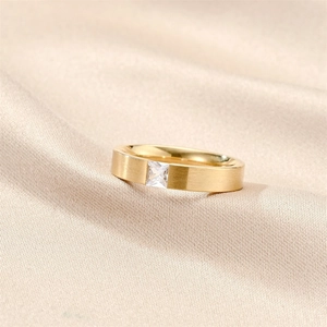 Macro detail of brushed gold titanium ring featuring a square-cut zircon on silk background