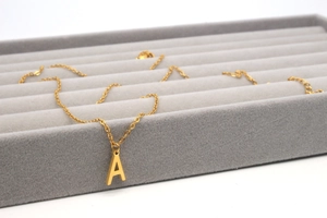 Makroaufnahme einer vergoldeten Edelstahlkette mit Buchstaben-A-Anhänger auf Samttablett