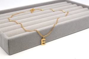 Detail einer goldenen Edelstahlkette mit poliertem Buchstaben-E-Anhänger auf Samt