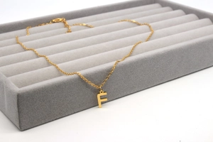 Detailaufnahme des goldenen Buchstabe-F-Anhängers an einer feinen Kette auf grauem Samt