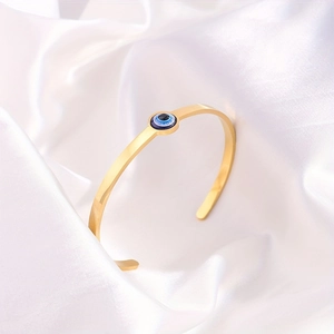 Verstellbarer goldener Edelstahl-Armreif mit Evil Eye auf elegantem weißem Seidenhintergrund