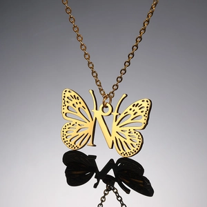Detailopname van een gouden vlinderhanger met de centrale letter N aan een verfijnde ketting