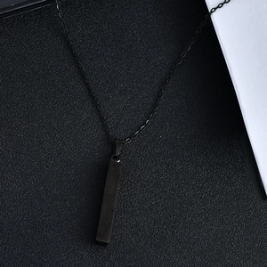Macro shot of minimalist matte black rectangular bar pendant with slim cross chain necklace