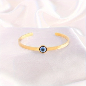 Makro-Detail des verstellbaren goldfarbenen Edelstahl-Armreifs mit Evil Eye auf Seide