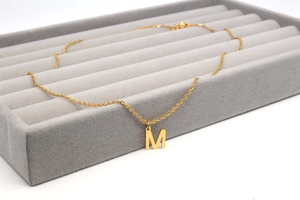 Detailansicht der goldenen M-Buchstabenkette auf einem grauen Samttablett für Schmuck