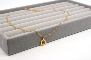 Detailansicht des goldenen Buchstaben Q Anhängers an einer feinen Kette auf Samt