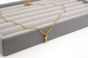 Detailansicht einer minimalistischen goldenen Kreuzkette auf einem grauen Samt-Schmuckdisplay