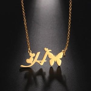Macro detail of a gold butterfly heart necklace with an engraved letter H on black surface