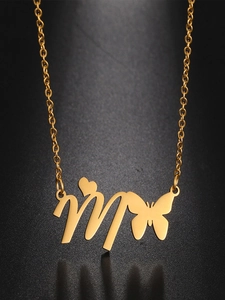 Detail of gold butterfly necklace with artistic heart letter M pendant on black surface