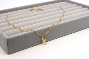 Detailansicht der goldenen Edelstahl-Halskette mit Buchstaben-X-Anhänger auf grauem Tablett