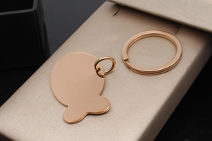 Polished rose gold stainless steel pet tag pendant on a textured jewelry box surface