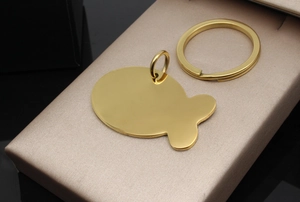 Close-up of a polished gold stainless steel fish-shaped pet tag on a champagne leather box