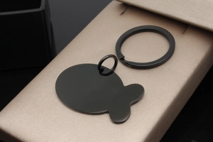 Close-up of black fish-shaped stainless steel pet ID tag on a textured gift box