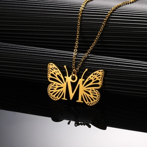 Detailopname van de gouden vlinder hanger letter M met fijne gravure aan de ketting