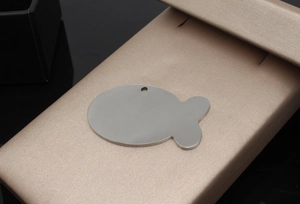 Macro shot of fish-shaped stainless steel pet ID tag with polished finish and top hole