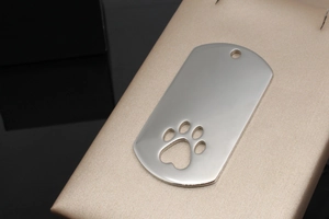 Macro view of shield-shaped stainless steel dog tag with hollowed out paw print design