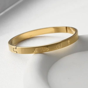 Gros plan d'un bracelet en titane doré mat avec gravure JESUS et motif religieux
