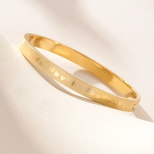 Polished gold titanium steel bangle with etched heart patterns and side clasp closure