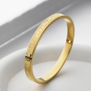 Detail of gold stainless steel bangle showing mesh texture, heart engraving and hinge closure