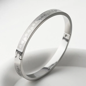 Macro detail of silver titanium steel bangle showing engraved heart pattern and hinge buckle