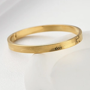 Close-up of gold titanium bracelet with love engraving and rose pattern details