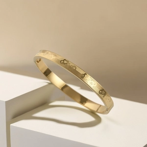Macro detail of gold love heart grid bangle featuring intricate etched metal texture