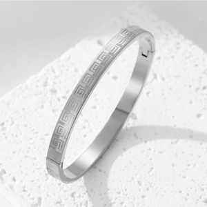 Close-up of titanium steel bracelet with Greek key pattern on a textured stone