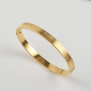 Close-up of gold titanium steel bangle with Greek key pattern and hinged clasp detail