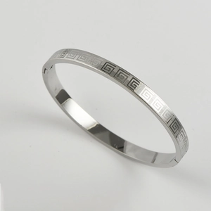 Macro shot of silver stainless steel bangle featuring geometric Greek key pattern and clasp
