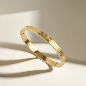 Macro detail of gold stainless steel bangle featuring engraved Greek key patterns