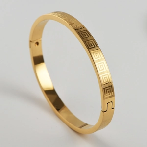 Macro detail of gold-plated stainless steel bangle with Greek meander engraved pattern