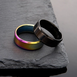 Anillos minimalistas de acero inoxidable arcoíris y negro sobre fondo de piedra oscura