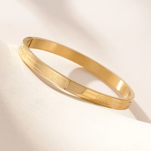 Polished gold stainless steel bangle featuring an engraved meander pattern with clasp